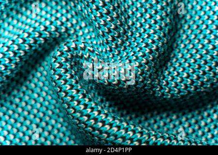 Twisted folds of synthetic knitted fabric with pattern elements of blue, black and white yarns close up. Multicolor patterned knitted fabric texture. Stock Photo
