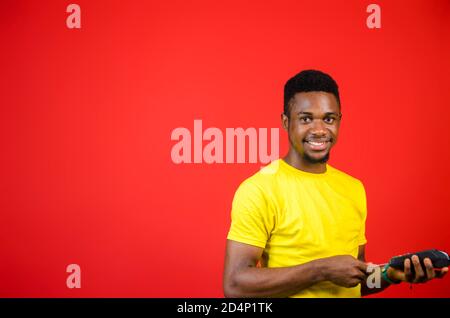 a young handsome african man wearing yellow cloth feeling excited as he holds his point of sales machine Stock Photo