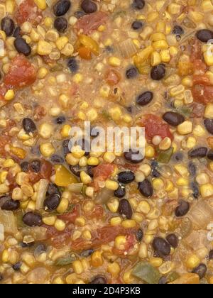 Vertical shot of yellow corns, tomatoes and black legume beans boiled in a water container Stock Photo