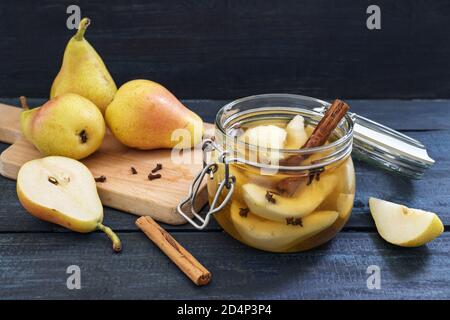 Preserving pears after the harvest with cinnamon and cloves in glass jars to have summer fruit also in winter, dark blue rustic wood, copy space, sele Stock Photo