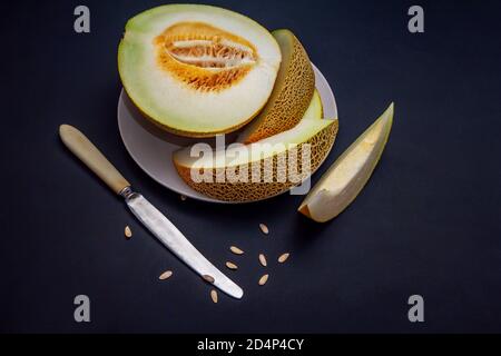 Fresh ripe juicy melon slices on a plate, knife and seeds on black table Stock Photo