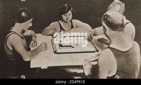 1924 - A family  (oddly dressed in swimming outfits?) playing Mah Jongg (various spellings e.g.  Mah-Jongg, Mahjong, Majong  etc). It became the latest craze in Britain in that year.  The game was developed during the Qing dynasty in China and has since spread throughout the world since the early 20th century. Stock Photo