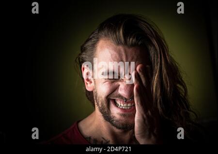 Young man with long hair covers his face while suffering from headache or migraine Stock Photo