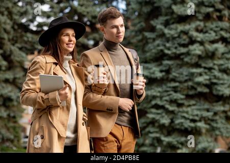 Young cheerful dates with glasses of coffee taking walk in urban environment Stock Photo