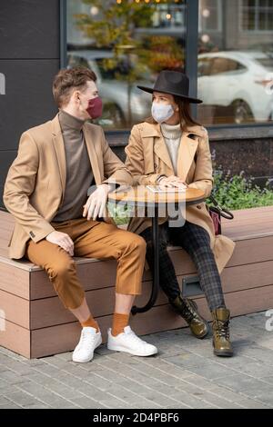 Young restful couple in protective masks and casualwear relaxing outdoors Stock Photo