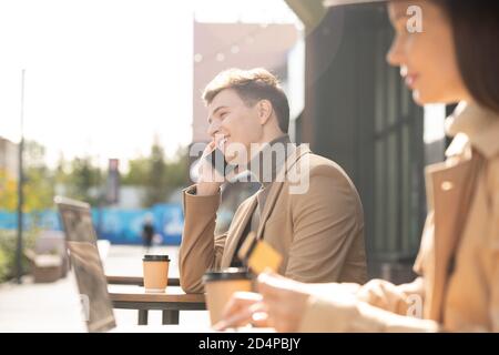 Young cheerful man in smart casualwear talking on mobile phone on sunny day Stock Photo