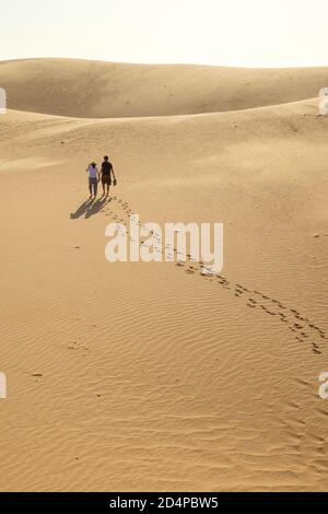 A couple is walking down the sand dunes in Mui ne during sunset. Stock Photo