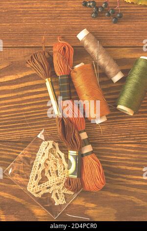 Floss yarn, laces, colored balls of thread and needles on a wooden background. Clothing designer's desktop. Top view of the autumn composition. Hobbies, crafts, knitting and sewing. Stock Photo