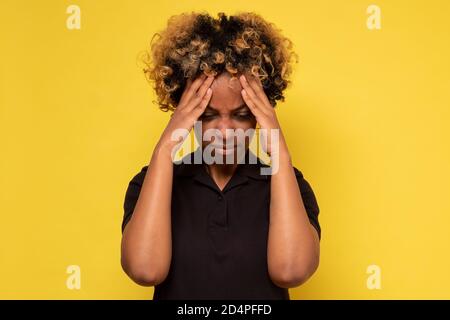 African woman with a headache holding hands on head, isolated on yellow background Stock Photo