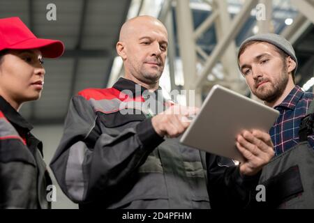 Serious bald mature foreman with tablet making presentation to subordinates Stock Photo