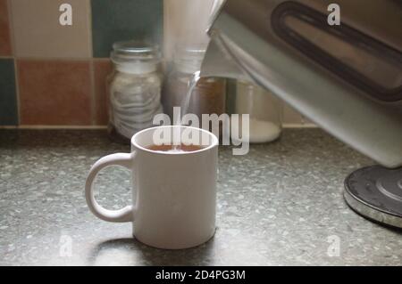 Pouring boiling water from a kettle into a mug to make a cup of tea Stock Photo