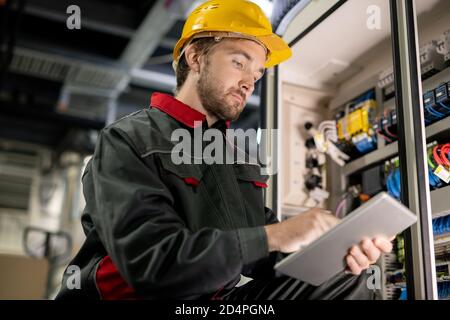 Young serious engineer in workwear and hardhat scrolling through technical data Stock Photo