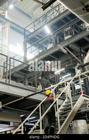 Foreman with tablet bending over staircase where female worker moving upwards Stock Photo