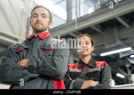 Two young successful workers of large modern factory crossing arms by chest Stock Photo