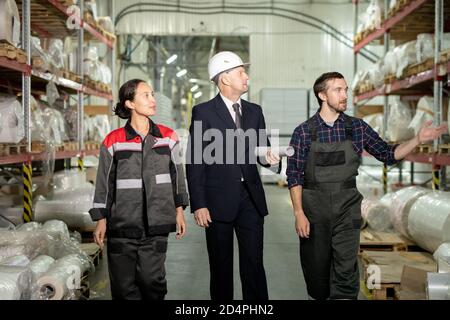 Two young engineers in workwear and mature director of factory in formalwear Stock Photo