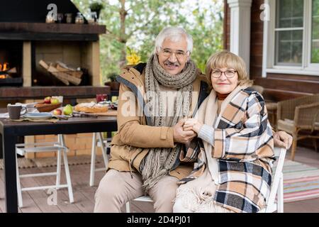 Happy senior affectionate grandparents in warm casualwear sitting by their house Stock Photo