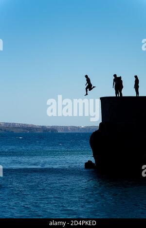 Group of friends jumping into mediterranean sea from rock cliff Stock Photo