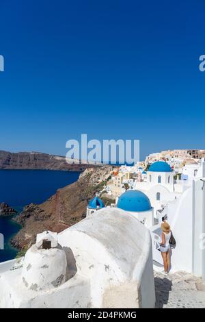 Woman taking snap of Santorini, with typical blue dome church, old whitewashed houses and caldera. Greek landscape on a sunny day Stock Photo