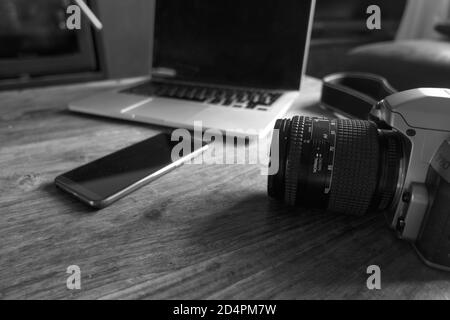 An old 35mm SLR camera on a coffee table alongside a modern smartphone and laptop. Stock Photo