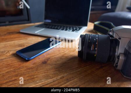 An old 35mm SLR camera on a coffee table alongside a modern smartphone and laptop. Stock Photo