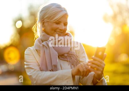 Senior woman using mobile phone outdoors in autumn Stock Photo