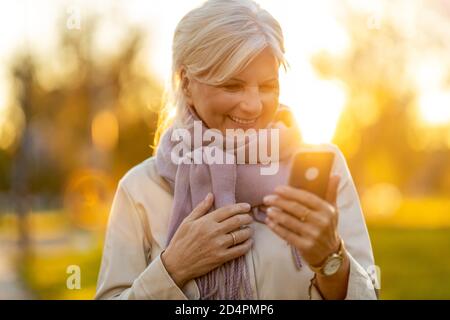 Senior woman using mobile phone outdoors in autumn Stock Photo