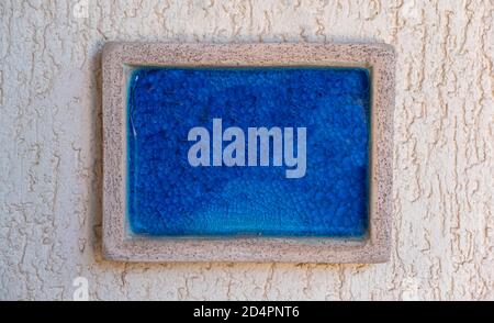 Board blank, empty, bright blue color sign, stone frame on beige rough plastered wall background, close up view. Sign template, copy space, Stock Photo