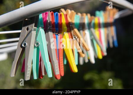 A colored clothes pegs hanging on a drying rack wire. A group of clothespin in line on stand at the sunny garden. Stock Photo