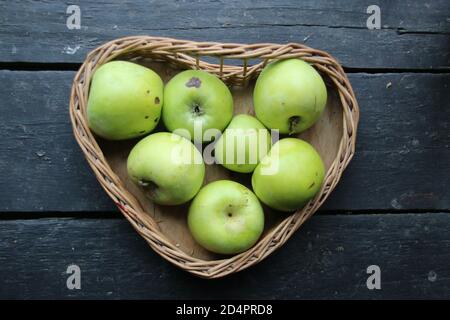 Ripe green apples on the table in a heart-shaped basket Stock Photo