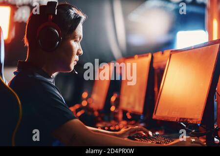 Side view of a focused asian guy, male professional cybersport gamer wearing headphones playing online video game, participating in eSport tournament Stock Photo