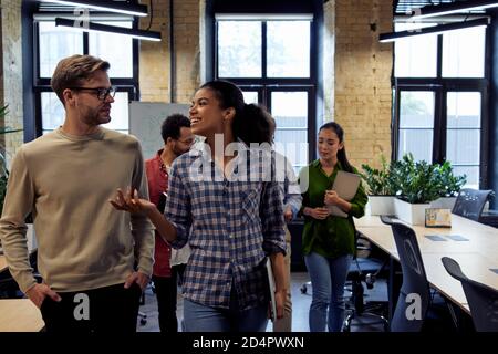 After team meeting. Two young diverse business people, male and female coworkers talking about something while walking in the modern office. Informal conversation at work Stock Photo