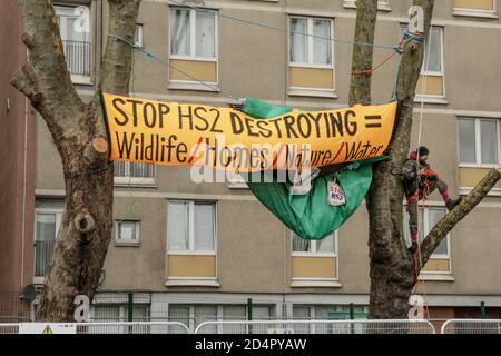 City of London, United Kingdom, 10th Oct 2020. Larch Maxey, longstanding environmentalist and tree protector from HS2 Rebellion and the STOP HS2 campaign, stands on one of the few trees left near the new high speed trainline works in Hampstead Rd. He is portraied near a banner urging to Stop the High Speed 2 train-line construction works and their destruction of wildlife sites, homes, nature and water throughout England. Credit: Sabrina Merolla / Alamy Live News. Stock Photo