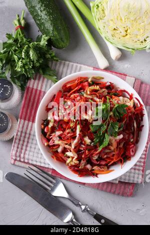 Salad from fresh vegetables: cabbage, beet, carrot, cucumber, onion and parsley in white bowl on gray background, Top view Stock Photo