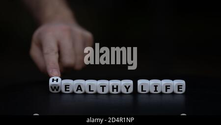 Hand turns dice and changes the expression 'wealthy life' to 'healthy life'. Stock Photo