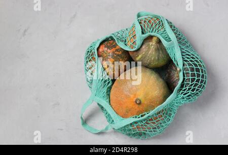 Various colorful pumpkins in turquoise string mesh bag on light background, Zero waste concept, Copy space, View from above. Stock Photo