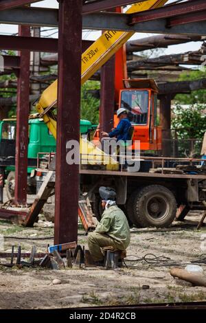 Welder in protective suit and mask on foreground. Crane and crane operator on background blurred. Construction of industrial building structure. Stock Photo