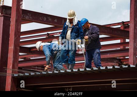 Shymkent, Kazakhstan. industrial building of chemical pharmaceutical plant Santo. Two workers and welder on roof makes reinforcement steel works. Stock Photo