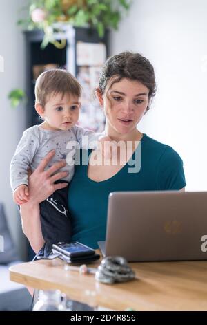 Woman using laptop computer with her 9 month old baby boy. Stock Photo