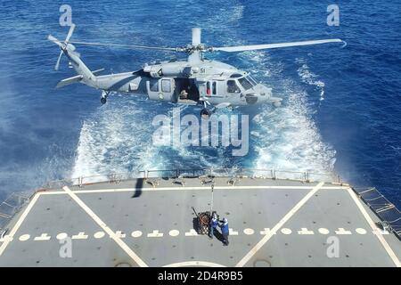 191228-N-PY805-1007 SOUTH CHINA SEA (Dec. 28, 2019) Personnel on the Henry J. Kaiser-class replenishment oiler USNS Pecos (T-AO 197) prepare to attached cargo to an MH-60S Sea Hawk assigned to Helicopter Sea Combat Squadron (HSC 23) during a vertical replenishment aboard the Independence-variant littoral combat ship USS Gabrielle Giffords (LCS 10). Gabrielle Giffords is on a rotational deployment to INDOPACOM, conducting operations, exercises and port visits throughout the region and working hull-to-hull with allied and partner navies to provide maritime security and stability, key pillars of Stock Photo