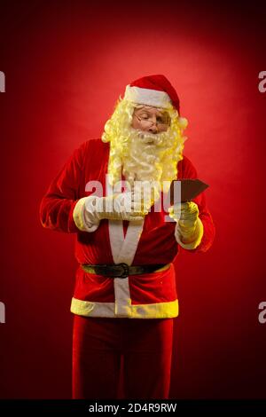 Santa Claus holds playing cards in his hands and poses on a dark red background Stock Photo