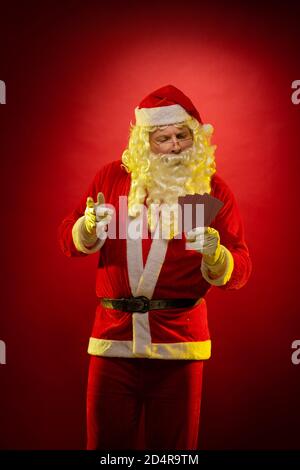Santa Claus holds playing cards in his hands and poses on a dark red background Stock Photo