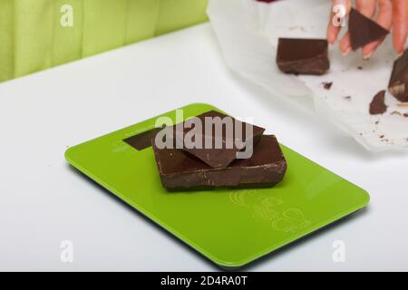 Chocolate on a kitchen scale. Woman breaks a bar of chocolate. Levington cake, stages of preparation. Stock Photo