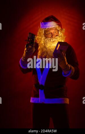 Male actor dressed as Santa Claus posing on a dark red background. Stock Photo