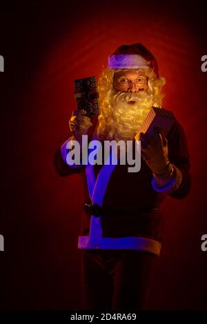 Male actor dressed as Santa Claus posing on a dark red background. Stock Photo