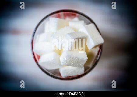 White sugar cubes in a measuring cup, conceptual image on sugar consumption excess. Stock Photo