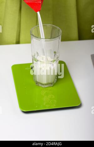 A woman pours milk into a glass on the kitchen scale. Levington cake, stages of preparation. Stock Photo