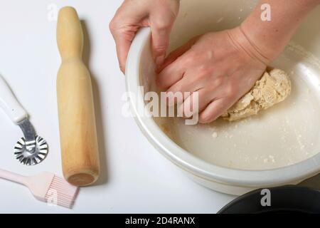 A woman kneads dough in a bowl. Cooking tools are nearby. Levington cake, stages of preparation. Stock Photo