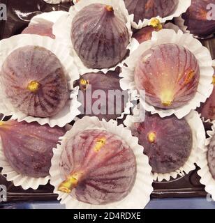 Group of purple fig fruits are on the white paper napkin tartlets decoration. Macro figs view in a circle. Ripe dark blue exotic fruits background. Stock Photo