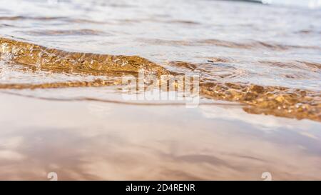 Small wave enters the beach during sunset which lights up the water with golden yellow color Stock Photo