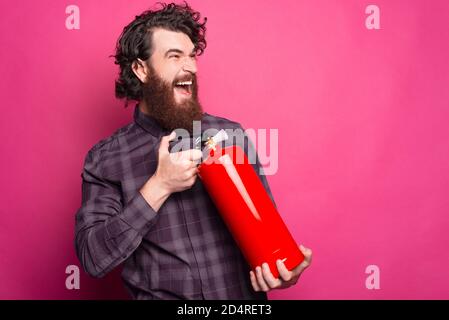 Photo of bearded man screaming and using Red Fire Extinguisher to stop fire. Stock Photo
